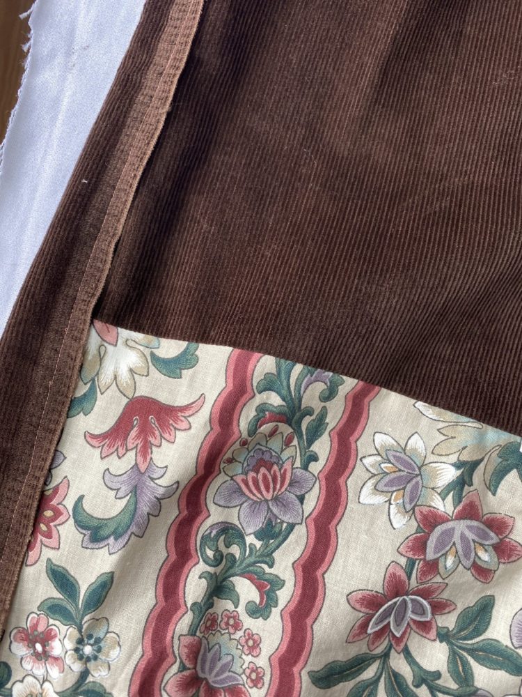 Detail shot of high waistedbrown corduroy trousers with vintage floral panel and raw selvedge edge