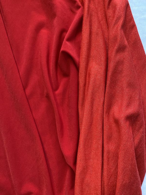 Detail shot of material of cotton red jersey batting jumper showing a slight difference in colour to sleeve body
