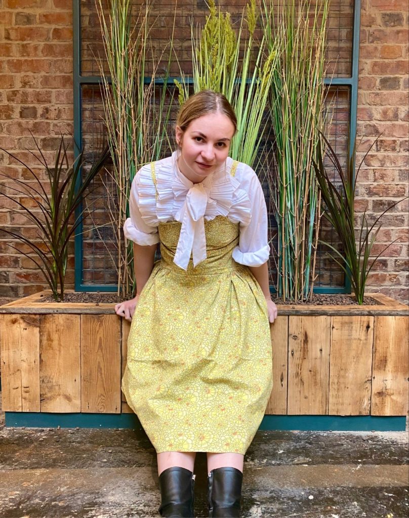 Evie Dainesfounder of Daines Atelier wearing Dress from Spring Summer 2022 Collection. The dress is made from a vintage 1970s fabric in bright yellow. It has a dropped waist and voluminous midi skirt.